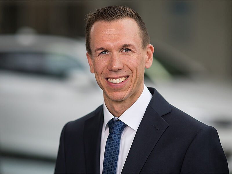 Kaltenbach Gruppe – Ein Mann in einem dunklen Anzug und blauer Krawatte lächelt in die Kamera. Er hat kurzes braunes Haar und steht im Freien vor einem unscharfen Hintergrund, möglicherweise in der Nähe von Kaltenbach Lüdenscheid. – BMW, MINI, KIA, BMW Motorrad & Honda Motorrad Partner in NRW