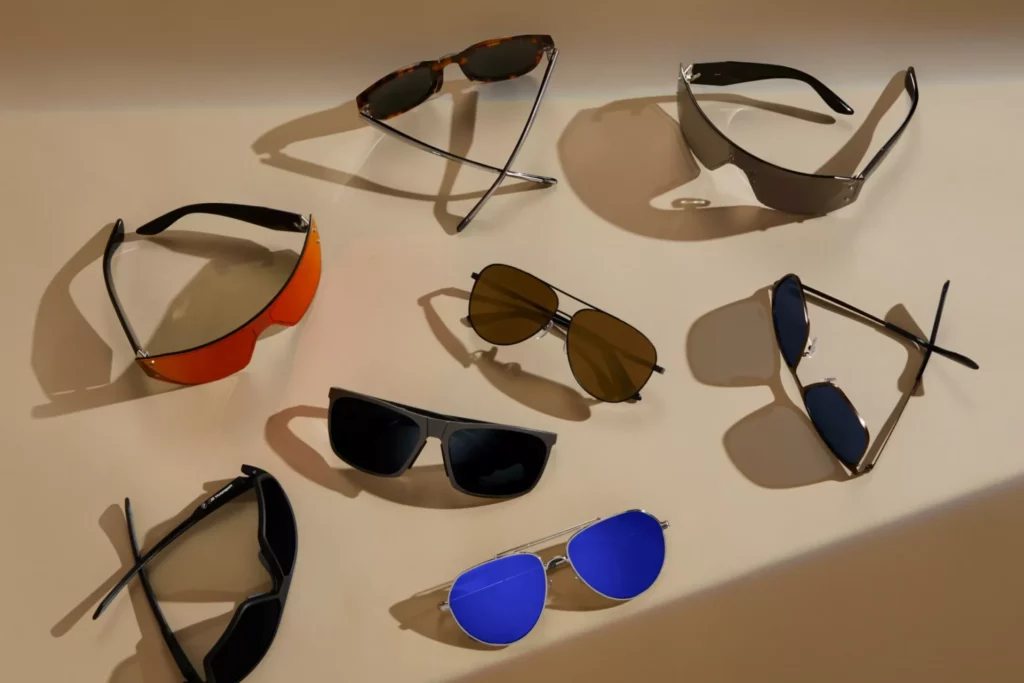 Kaltenbach Gruppe – Acht Sonnenbrillen mit unterschiedlichen Fassungen und Gläsern, darunter Schwarz, Braun, Orange und Blau, sind auf einer beigen Fläche mit weichen Schatten angeordnet und verleihen Ihrer Markenwelt-Kollektion einen Hauch von BMW-Raffinesse. – BMW, MINI, KIA, BMW Motorrad & Honda Motorrad Partner in NRW