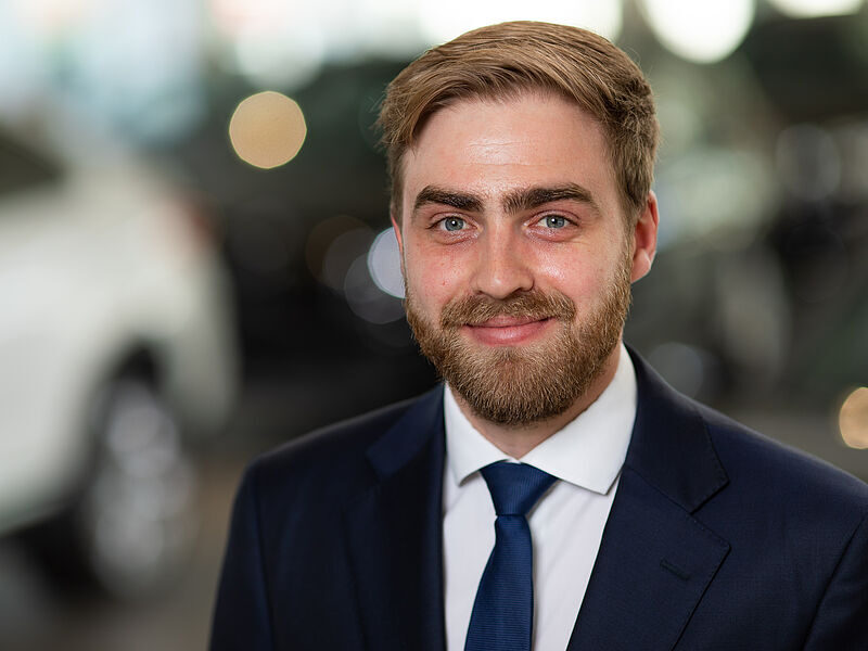 Kaltenbach Gruppe – Ein Mann mit hellbraunem Haar und Bart, der einen marineblauen Anzug, ein weißes Hemd und eine blaue Krawatte trägt, lächelt vor einem unscharfen Hintergrund in die Kamera - ein professioneller Moment in Kaltenbach-Wiehl. – BMW, MINI, KIA, BMW Motorrad & Honda Motorrad Partner in NRW