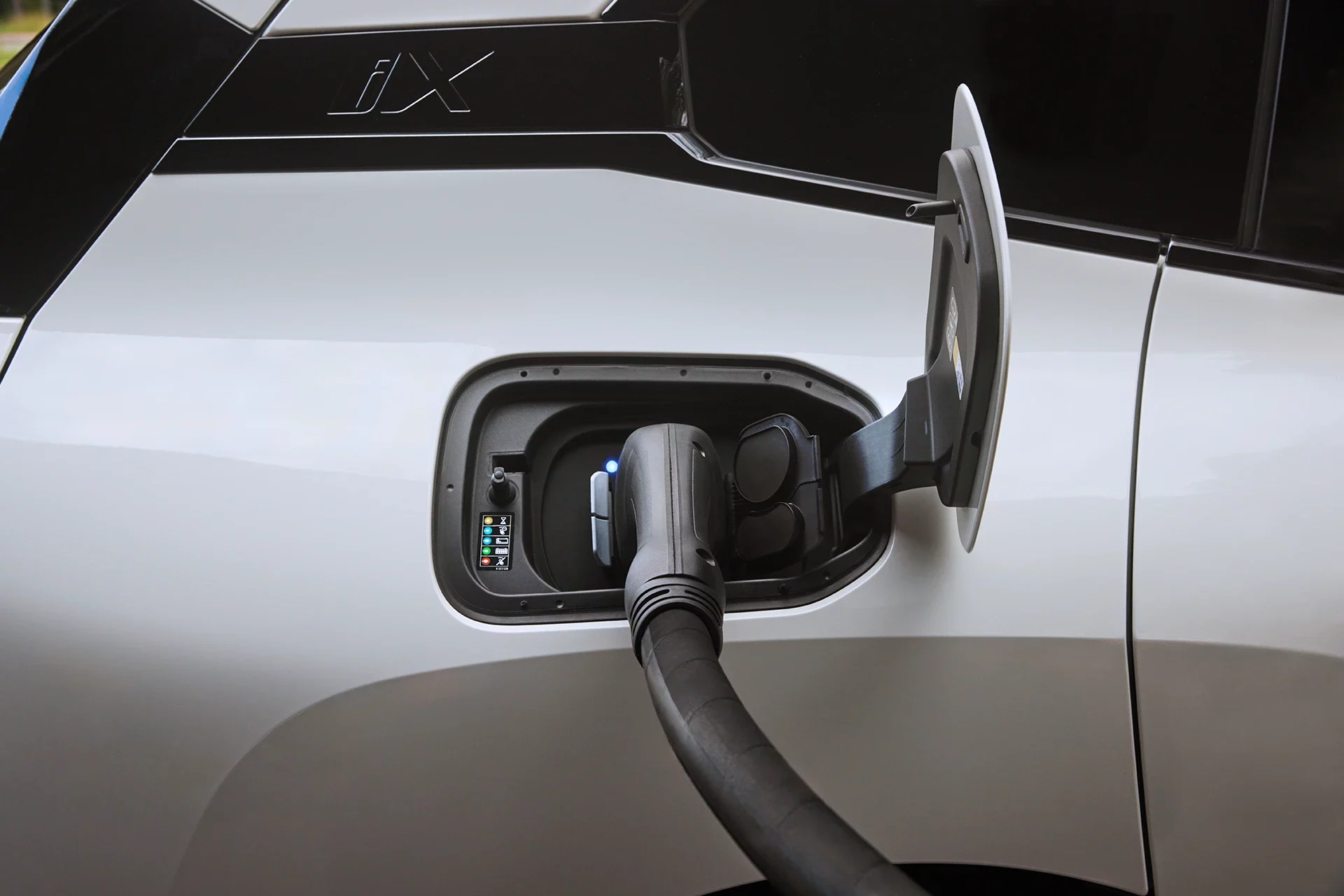 Kaltenbach Gruppe – Nahaufnahme eines Elektrofahrzeugs beim Aufladen, wobei das Ladekabel in den Anschluss des Fahrzeugs eingesteckt ist. Die Buchstaben IX sind auf der Außenseite in der Nähe der Ladestation zu sehen und weisen auf Premium-Zubehör und Teile hin. – BMW, MINI, KIA, BMW Motorrad & Honda Motorrad Partner in NRW