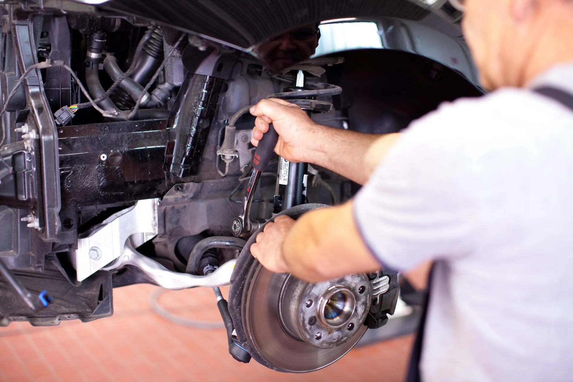 Kaltenbach Gruppe – Ein Mechaniker führt in einer Werkstatt eine Reparatur an der Vorderradbremse eines Autos durch und konzentriert sich dabei auf die freigelegte Radnabe und die Bremsscheibe nach einem Unfall. – BMW, MINI, KIA, BMW Motorrad & Honda Motorrad Partner in NRW
