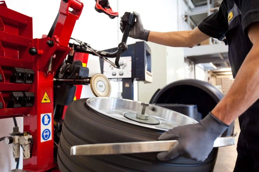 Kaltenbach Gruppe – In einer Autowerkstatt benutzt ein Mechaniker mit Handschuhen eine spezielle Ausrüstung für die Reparatur und montiert mit einer Reifenwechselmaschine fachmännisch einen Reifen auf eine Felge. – BMW, MINI, KIA, BMW Motorrad & Honda Motorrad Partner in NRW