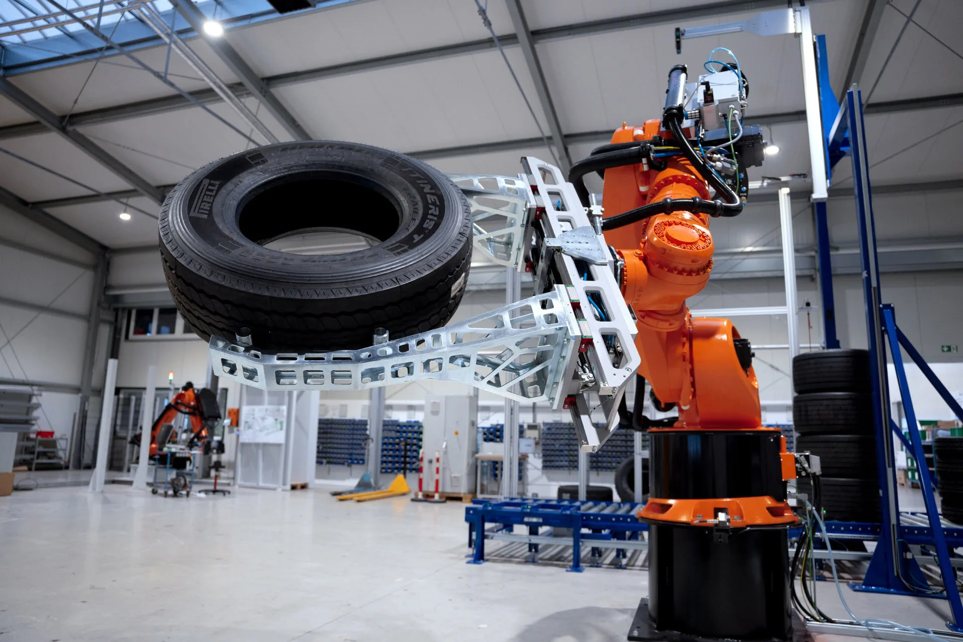 Kaltenbach Gruppe – Ein Industrieroboterarm hält einen großen Autoreifen in einer modernen Fabrik, in der Geräte und Reifenstapel auf laufende Reparaturarbeiten hindeuten; ein weiterer Roboter arbeitet im Hintergrund und sorgt für Effizienz nach einem Unfall. – BMW, MINI, KIA, BMW Motorrad & Honda Motorrad Partner in NRW