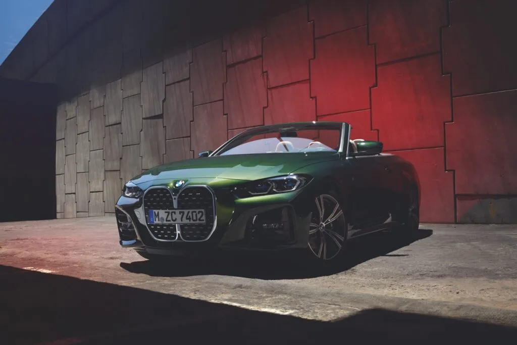 Kaltenbach Gruppe – Ein grünes BMW Cabrio mit offenem Verdeck ist in einem schattigen Stadtgebiet geparkt, das teilweise vom Sonnenlicht beleuchtet wird. Die moderne, rot gefärbte Wand im Hintergrund deutet auf nahegelegene Serviceleistungen oder Termine für Stadtfahrer hin. – BMW, MINI, KIA, BMW Motorrad & Honda Motorrad Partner in NRW