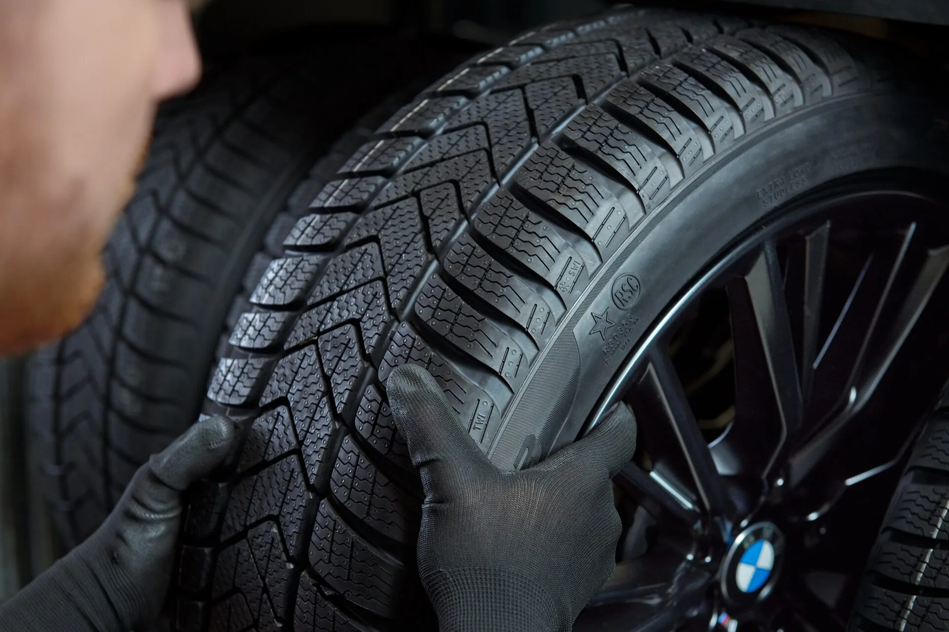 Kaltenbach Gruppe – Eine Person mit schwarzen Handschuhen montiert oder prüft einen BMW-Reifen und konzentriert sich dabei auf das detaillierte Reifenprofil und das BMW-Logo auf der Felge. – BMW, MINI, KIA, BMW Motorrad & Honda Motorrad Partner in NRW
