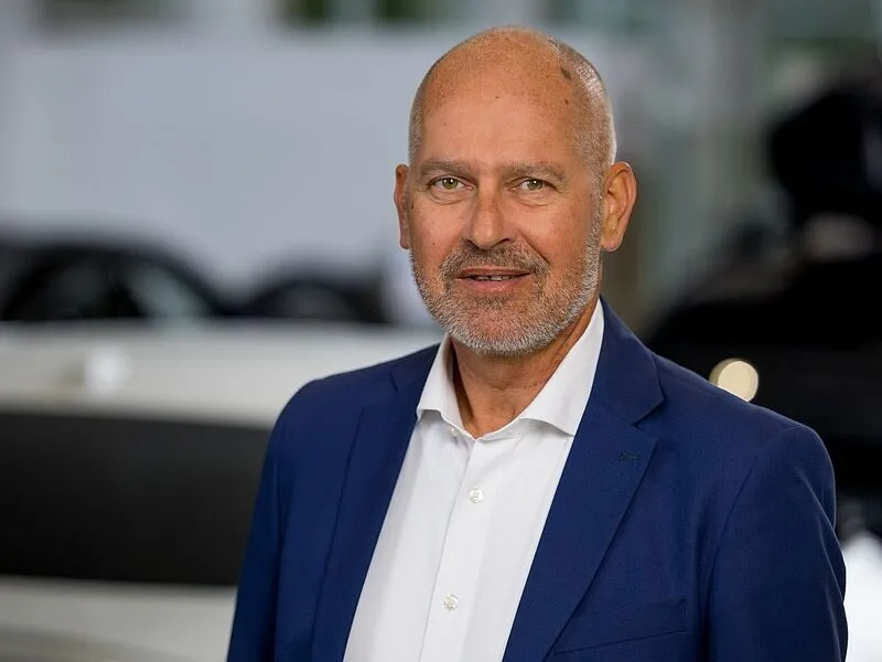 Kaltenbach Gruppe – Ein Mann mittleren Alters mit Glatze und Bart, der eine blaue Anzugsjacke und ein weißes Hemd trägt, steht in einem Haus in Kaltenbach Overath vor einem unscharfen Hintergrund. – BMW, MINI, KIA, BMW Motorrad & Honda Motorrad Partner in NRW