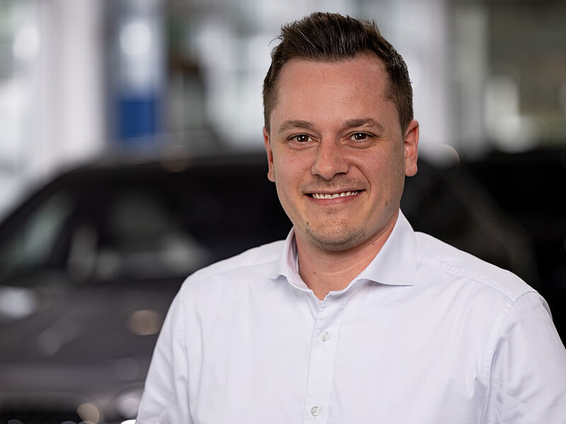 Kaltenbach Gruppe – Ein Mann mit kurzen braunen Haaren, der ein weißes Hemd trägt, lächelt in die Kamera. Der unscharfe Hintergrund deutet auf ein Auto und eine Innenraumumgebung hin, möglicherweise in Kaltenbach Waldbröl. – BMW, MINI, KIA, BMW Motorrad & Honda Motorrad Partner in NRW