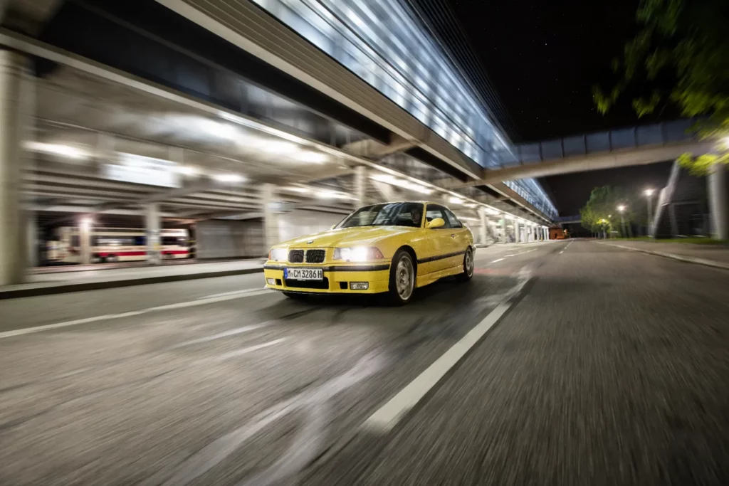 Kaltenbach Gruppe – Ein gelber BMW-Sportwagen, Teil der Kaltenbach Classic, rast durch eine leere nächtliche Stadtstraße, mit verschwommenen Lichtern und modernen Gebäuden im Hintergrund, die ein Gefühl von Bewegung erzeugen. – BMW, MINI, KIA, BMW Motorrad & Honda Motorrad Partner in NRW