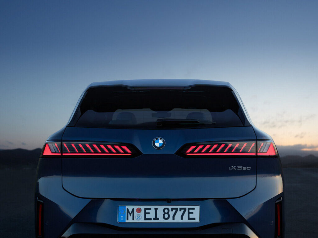 Kaltenbach Gruppe – Rückansicht eines blauen BMW iX Elektro-Geländewagens in der Dämmerung, mit leuchtenden roten Rücklichtern, einem klaren Himmel im Hintergrund und einem europäischen Nummernschild - geparkt neben einem iX3 für ein eindrucksvolles Duo moderner Elektrofahrzeuge. – BMW, MINI, KIA, BMW Motorrad & Honda Motorrad Partner in NRW