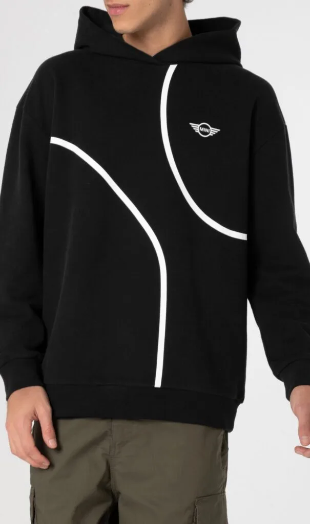 Kaltenbach Gruppe – Eine Person trägt einen schwarzen Kapuzenpullover mit weißen geschwungenen Linien und einem kleinen MINI-Logo auf der Brust, gepaart mit einer olivgrünen Cargohose. Der Hintergrund ist einfarbig und das Gesicht der Person ist teilweise außerhalb des Rahmens. – BMW, MINI, KIA, BMW Motorrad & Honda Motorrad Partner in NRW