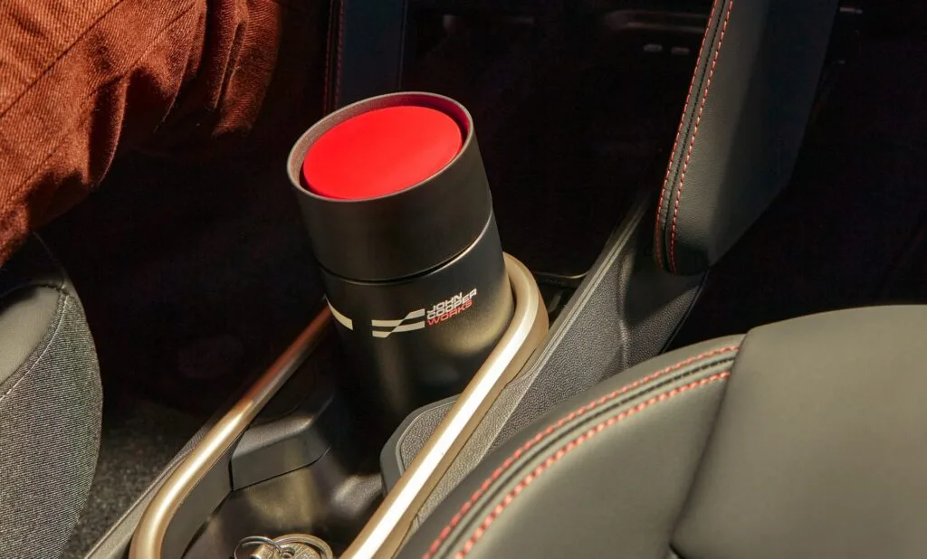Kaltenbach Gruppe – Ein schwarzer Reisebecher mit rotem Deckel steht in einem Getränkehalter im Auto neben einem Schlüsselbund, umgeben von schwarzen Sitzen mit roten Nähten und einer braunen Hose. – BMW, MINI, KIA, BMW Motorrad & Honda Motorrad Partner in NRW