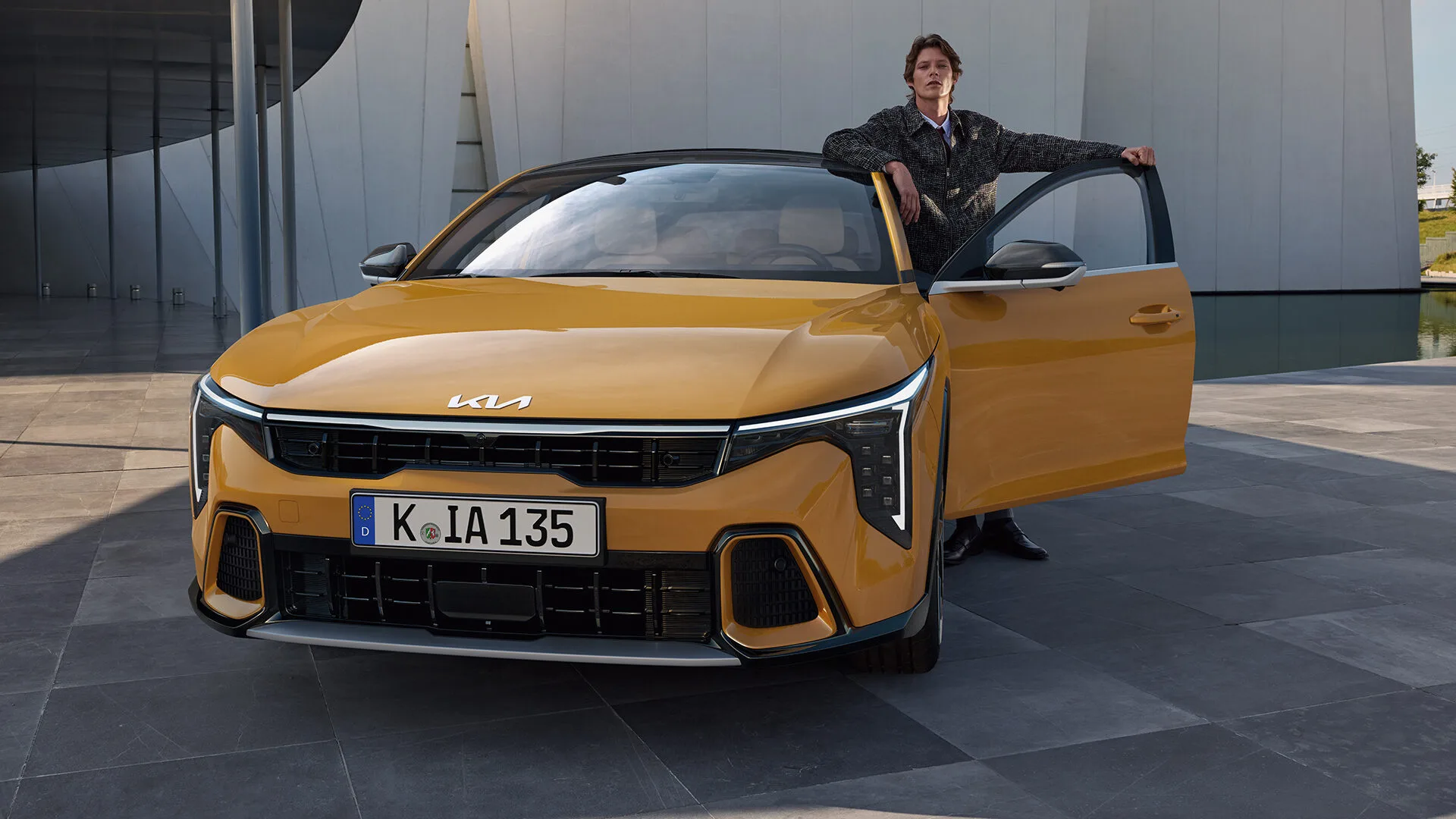 Kia K4 in Gelb von vorn, ein Mann steht in der geöffneten Fahrertür