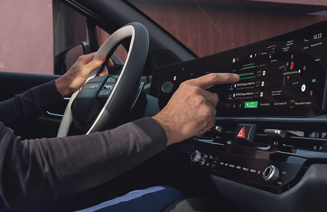 Cockpit des Kia Sportage mit gewölbtem Display und Hand am Lenkrad